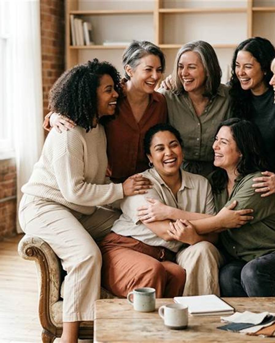 Grupo de mujeres riendo y abrazadas en un living calido, compartiendo un momento cercano